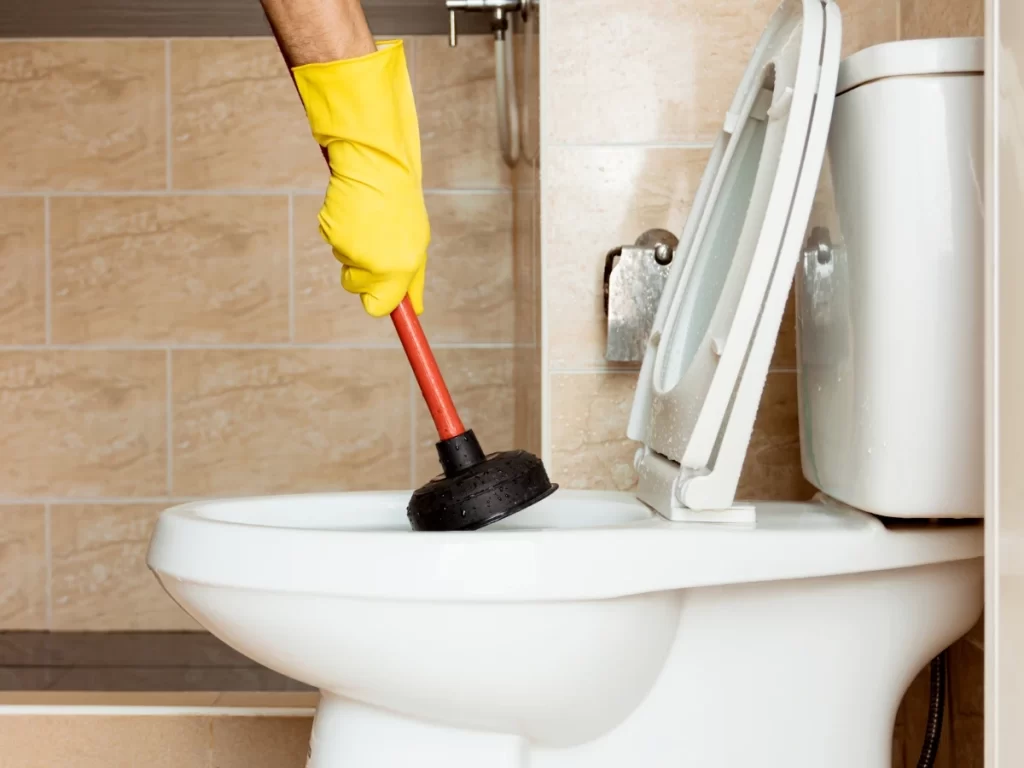 image of a hand using a plunger to showing how to unclog a toilet