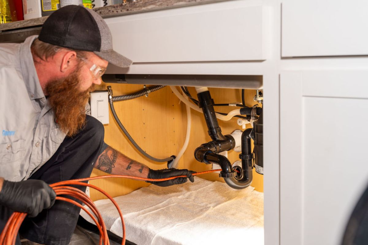 Done Rite Services professional plumber inspecting pipes under a kitchen sink.