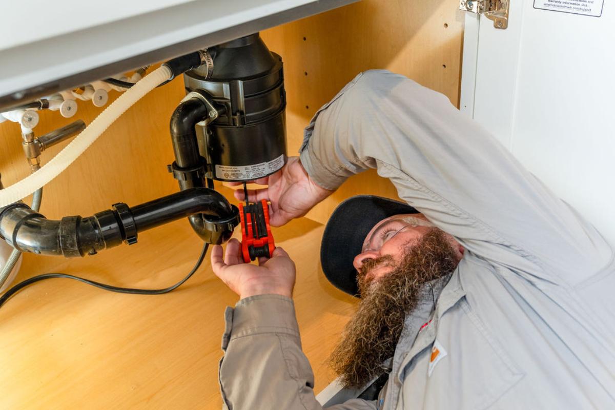 Done Rite Services plumber inspecting the plumbing system under a kitchen sink.