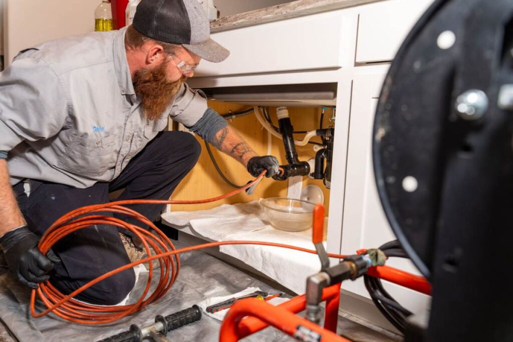 Expert plumber from Done Rite Services using a drain snake to remove a clog under a sink drain