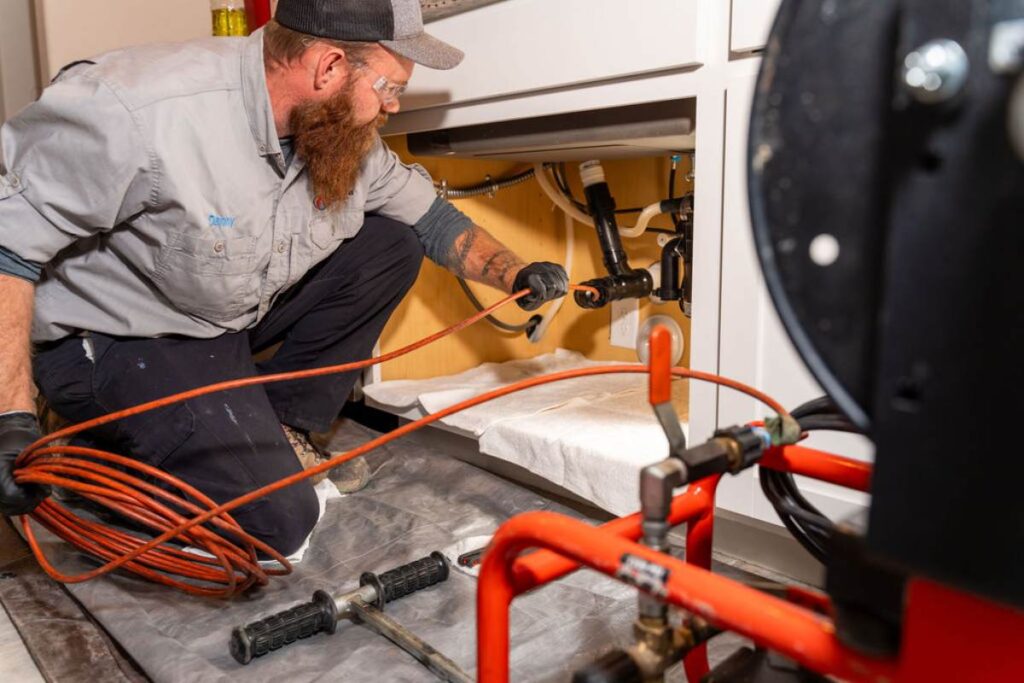 Done Rite Services professional plumber using a drain snake to remove a clog under a sink drain