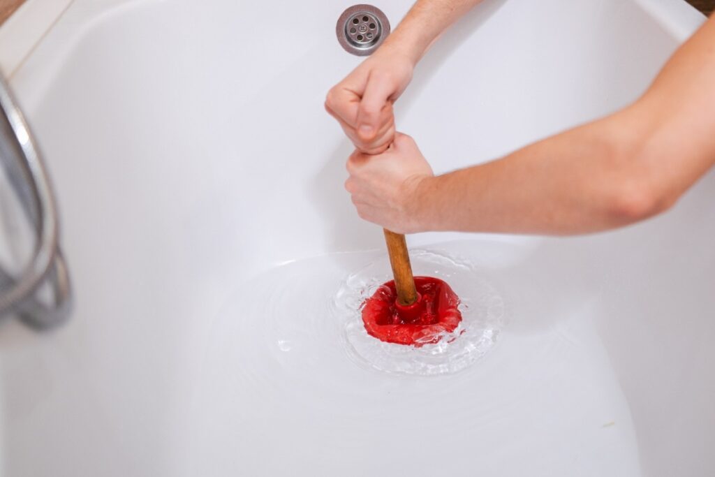 Using a plunger to unclog a bathtub drain.