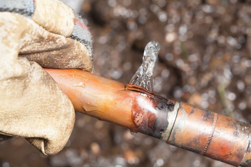 Close-up of a damaged pipe with visible cracks and water leaking.