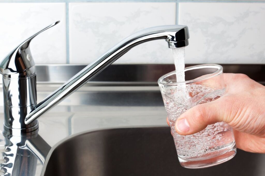 Close-up of a glass being filled with water from a running faucet for water quality testing.